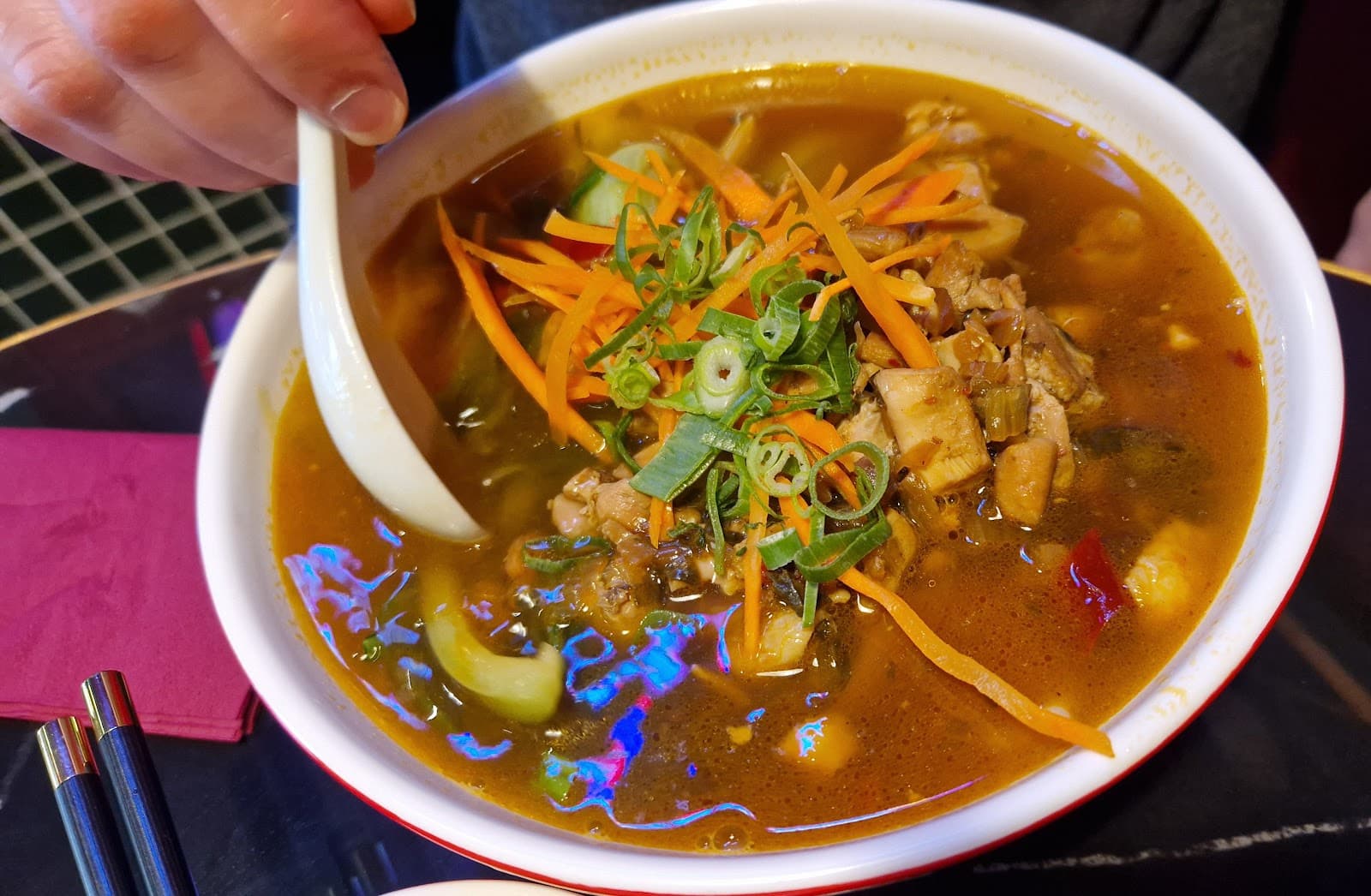 Scharfe Suppe mit Gemüse, ein Löffel wird gehalten